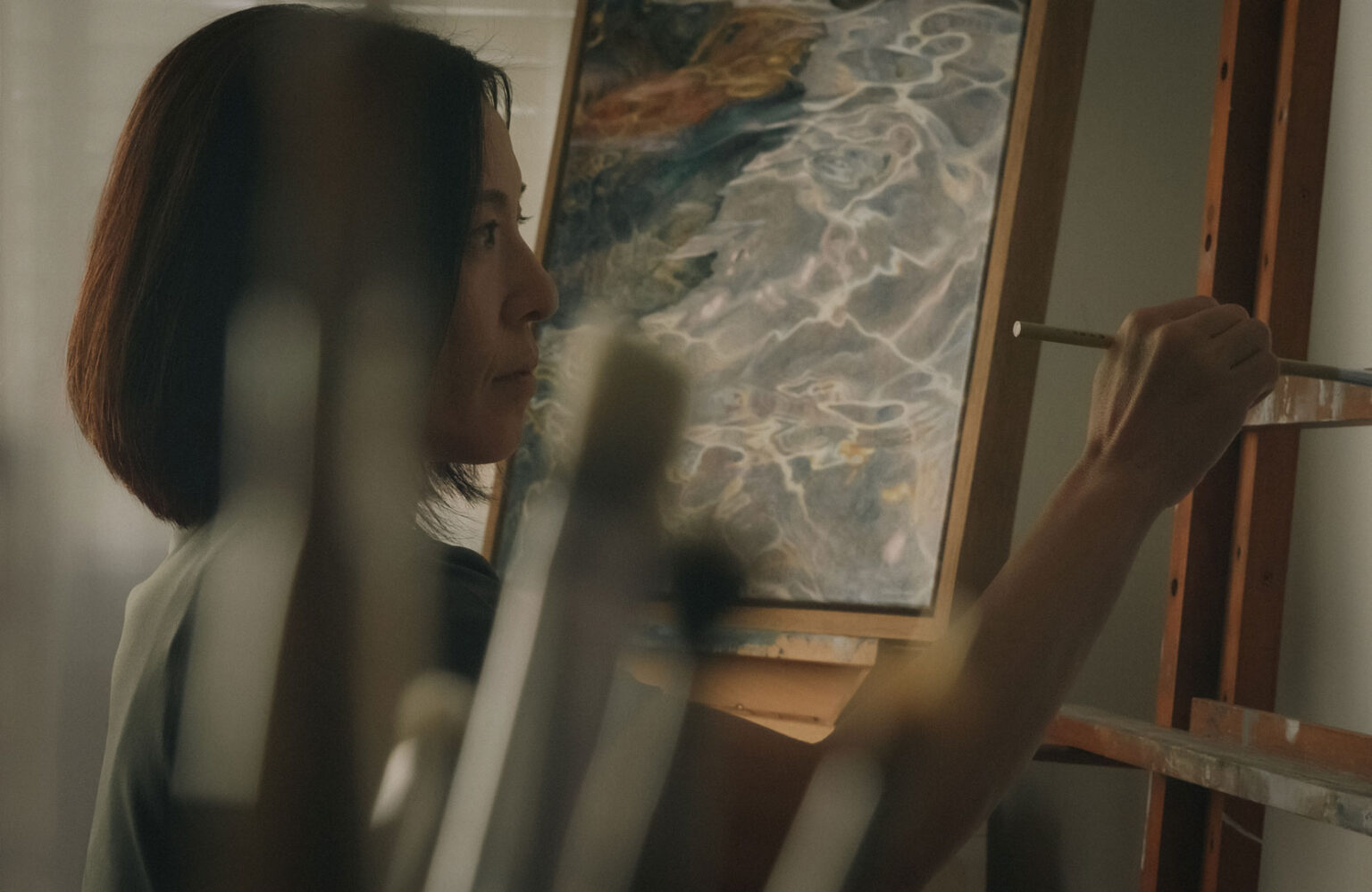 Looking through blurry paintbrushes to an artist focusing on their painting